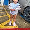blue_door, car, child, clothing, concrete, daylight, face, hair, open_car_door, outdoor, parking_lot, person, red_line, shoes, sidewalk, socks, standing, toddler, urban, yellow_lines