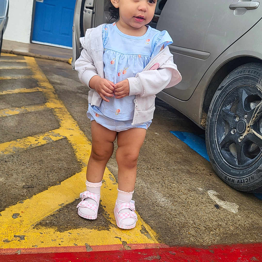 Mellodie-Grace is registered to the contest to win money with this photo: toddler, child, parking_lot, car, open_car_door, blue_door, sidewalk, yellow_lines, red_line, socks, shoes, clothing, outdoor, person, concrete, hair, face, standing, daylight, urban