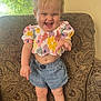 Ava joined the competition — help win amazing prizes! toddler, child, smiling, standing, armchair, floral_top, denim_shorts, indoor, natural_light, happy, blond_hair, messy_hair, patterned_furniture, window, playful, cute, person, young_child, casual_clothing, home