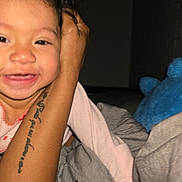 Rachell Mendoza is registered to the contest to win money with this photo: toddler, smile, child, curly_hair, earrings, tattoo, arm, blanket, plush_toy, blue_toy, indoor, bedroom, happy, person, face, clothing, pink_shirt, cozy, closeup, portrait