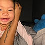 toddler, smile, child, curly_hair, earrings, tattoo, arm, blanket, plush_toy, blue_toy, indoor, bedroom, happy, person, face, clothing, pink_shirt, cozy, closeup, portrait