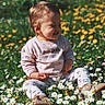 child, toddler, smiling, sitting, flowers, daisies, grass, outdoor, nature, sunlight, spring, greenery, happy, cute, baby_clothes, field, blossoms, playful, daylight, casual