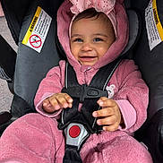 Illiana joined the competition — help win amazing prizes! baby, child, car_seat, pink_onesie, headband, bow, smile, happy, infant, safety_harness, cute, indoors, portrait, young_child, clothing, person, baby_clothes, seat, hands, face