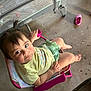 Adelina joined the competition — help win amazing prizes! toddler, child, sitting, chair, pink, yellow_shirt, green_shorts, pony_tail, indoor, playpen, shoe, concrete_floor, curious, looking_up, small_chair, casual, baby, person, footwear, furniture