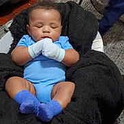 Kendrick is registered to the contest to win money with this photo: baby, infant, sleeping, portrait, blue_outfit, mittens, socks, plush_chair, seated, indoors, cozy, face, closed_eyes, dark_hair, smiling, household, fan, carpet, wood_floor, photography
