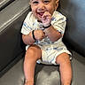 baby, smiling, infant, child, cute, sitting, white_outfit, vehicles_pattern, dimples, happy, leather_couch, barefoot, close_up, portrait, indoor, skin, face, hand, foot, young_child