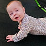 Raven is registered to the contest to win money with this photo: baby, infant, smiling, floral_onesie, trampoline, outdoor, sunlight, happy, child, face, crawling, playtime, black_mat, green_edges, cute, portrait, young, person, daylight, baby_clothing