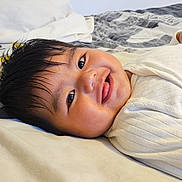 Kieran joined the competition — help win amazing prizes! baby, smiling, tongue_out, bed, white_clothing, heart_patch, lying_down, blanket, pillow, child, cute, indoors, face, happy, infant, person, soft_texture, home, sleepwear, young
