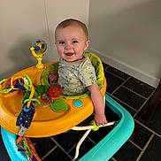 Stetson is registered to the contest to win money with this photo: baby, child, walker, toy, smile, happy, indoor, floor, tiles, clothing, person, infant, bright, play, seat, plastic, colorful, face, cute, young