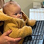 baby, child, infant, keyboard, hand, jacket, fur_clothing, computer_accessory, indoor, person, technology, curious, seated, young_child, close_up, desk, office, typing, supporting_hand, fluffy_jacket