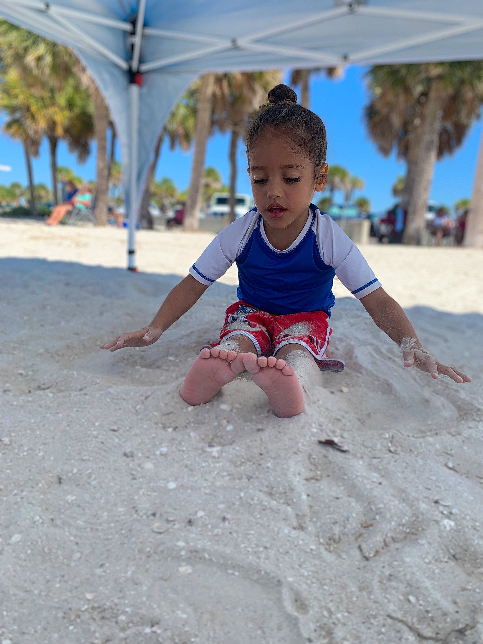 Neiko is registered to the contest to win money with this photo: barefoot, beach, body_of_water, child, foot, fun, happy, landscape, leisure, ocean, people_on_beach, person, recreation, sand, shade, sitting, sky, soil, t_shirt, toddler