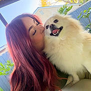 Peety Papa Bear is registered to the contest to win money with this photo: person, dog, smiling, outdoor, sunlight, red_hair, fluffy_dog, kiss, happy, fence, tree, greenery, pet, closeup, portrait, animal, nature, canine, affection, daylight