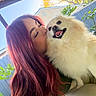person, dog, smiling, outdoor, sunlight, red_hair, fluffy_dog, kiss, happy, fence, tree, greenery, pet, closeup, portrait, animal, nature, canine, affection, daylight