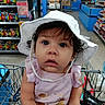 Luna joined the competition — help win amazing prizes! toddler, child, white_hat, shopping_cart, grocery_store, curly_hair, pink_clothing, facial_expression, indoor, retail, products, shelves, person, young_child, cute, hat, shopping, baby, eyes, store_aisle