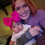 Kyndall is registered to the contest to win money with this photo: baby, bow, candid, casual, closeup, clothing, expression, face, hair, hand, happy, holding, indoor, person, pink_bow, portrait, seated, smile, woman, wrist_brace