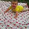 Nova is registered to the contest to win money with this photo: baby, child, yellow_clothing, blanket, patterned_blanket, outdoor, grass, dirt, crawling, smiling, happy, infant, face, head, person, nature, playtime, cute, young_child, daylight