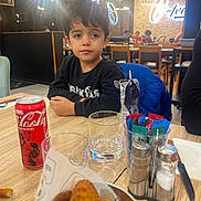 Göktuğ a rejoint le concours — aidez-le/la à gagner de superbes lots ! child, boy, restaurant, table, food, drink, coca_cola, glass, napkin, salt_shaker, pepper_shaker, condiments, jacket, sitting, indoor, lights, people, reflection, wooden_table, casual