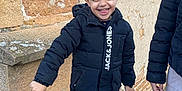 Göktuğ a rejoint le concours — aidez-le/la à gagner de superbes lots ! child, boy, smiling, jacket, black_jacket, jeans, sneakers, outdoor, stone_wall, standing, happy, casual_clothing, daylight, person, fashion, young, playful, fun, portrait, urban