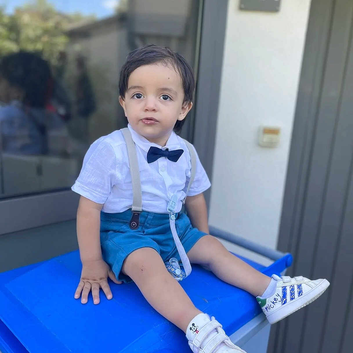Göktuğ participe au concours pour gagner de l'argent avec cette photo : blue_shorts, bow_tie, boy, casual, child, curious, daylight, door, house_number, mickey_mouse, outdoor, reflection, shoes, sidewalk, sitting, suspenders, toddler, trash_bin, white_shirt, window
