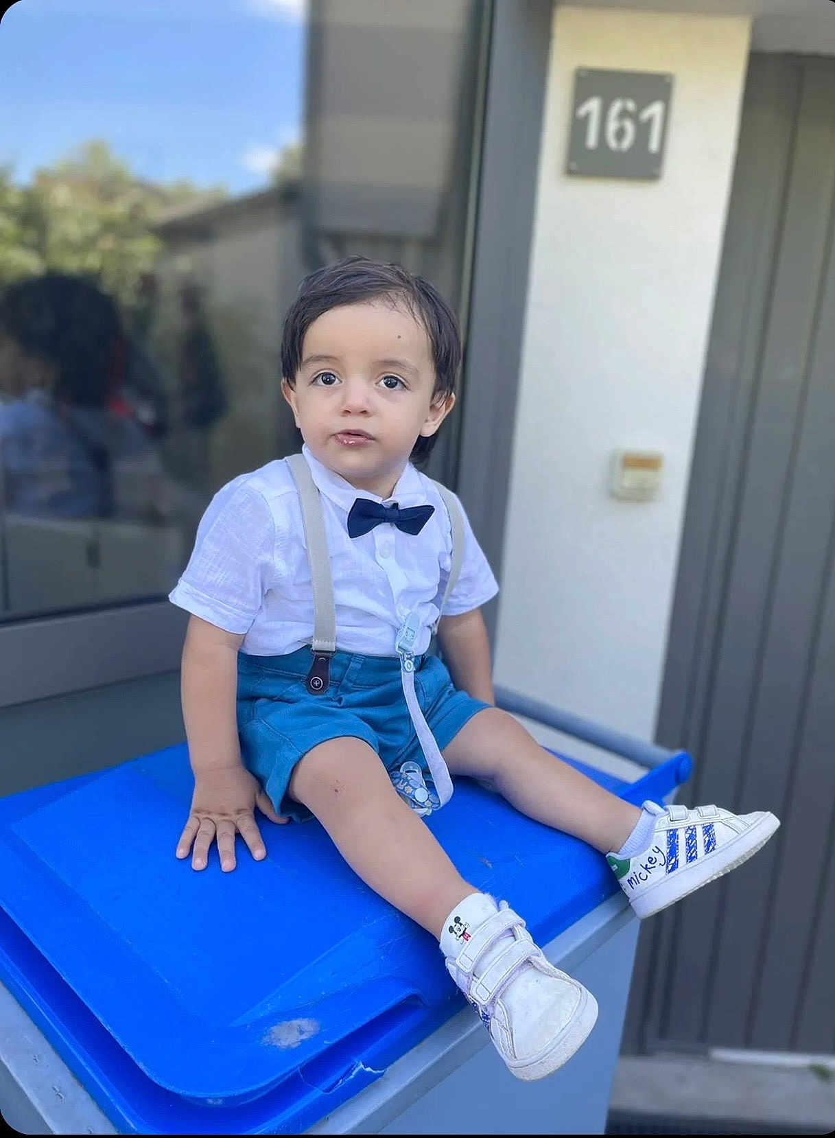 Göktuğ participe au concours pour gagner de l'argent avec cette photo : toddler, child, boy, sitting, blue_shorts, white_shirt, bow_tie, suspenders, mickey_mouse, shoes, outdoor, trash_bin, door, house_number, curious, casual, daylight, window, reflection, sidewalk