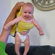 Diègo participe au concours pour gagner de l'argent avec cette photo : baby, child, towel, diaper, smiling, happy, arm, hand, adult, green_shirt, couch, clock, wall, indoor, furniture, person, skin, foot, head, home
