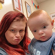 Joshua Corey is registered to the contest to win money with this photo: baby, bib, casual, child, clothing, colorful_flags, curious, expression, face, framed_letters, holding, indoor, person, playful, portrait, red_hair, room, selfie, wall_art, woman