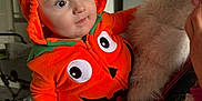 Archie joined the competition — help win amazing prizes! baby, baby_outfit, child, costume, cute, face, fur, glasses, happy, holding, human, indoor, jacket, orange_clothing, person, portrait, pumpkin_costume, smile, striped_pants, woman