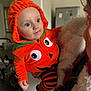 baby, baby_outfit, child, costume, cute, face, fur, glasses, happy, holding, human, indoor, jacket, orange_clothing, person, portrait, pumpkin_costume, smile, striped_pants, woman