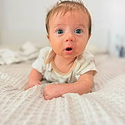 Enzo is registered to the contest to win money with this photo: baby, infant, child, portrait, face, blue_eyes, wide_eyed, surprised, open_mouth, smiling, lying_down, crawling, blanket, bed, indoors, close_up, soft_lighting, brown_hair, casual_clothing, photography
