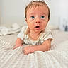 baby, infant, child, portrait, face, blue_eyes, wide_eyed, surprised, open_mouth, smiling, lying_down, crawling, blanket, bed, indoors, close_up, soft_lighting, brown_hair, casual_clothing, photography