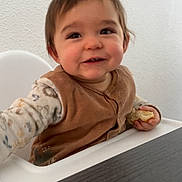 Paul participe au concours pour gagner de l'argent avec cette photo : toddler, child, high_chair, smiling, bread, food, indoor, person, clothing, sleeve, vest, table, happy, face, hand, hair, white_wall, furniture, young_child, casual