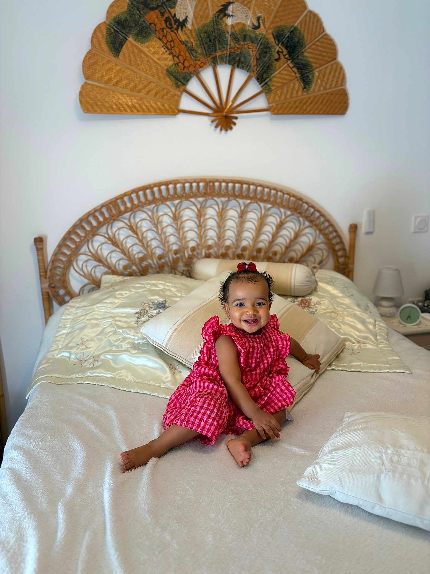 Neydee a rejoint le concours — aidez-le/la à gagner de superbes lots ! toddler, child, smiling, bed, pillow, red_dress, curly_hair, indoors, home, headboard, decorative_fan, blanket, furniture, cute, happy, sitting, cozy, room, baby, portrait