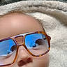baby, face, glasses, sunglasses, reflection, blanket, soft_texture, carpet, indoor, close_up, child, infant, cute, serious_expression, head, person, wearing, eyewear, humor, portrait