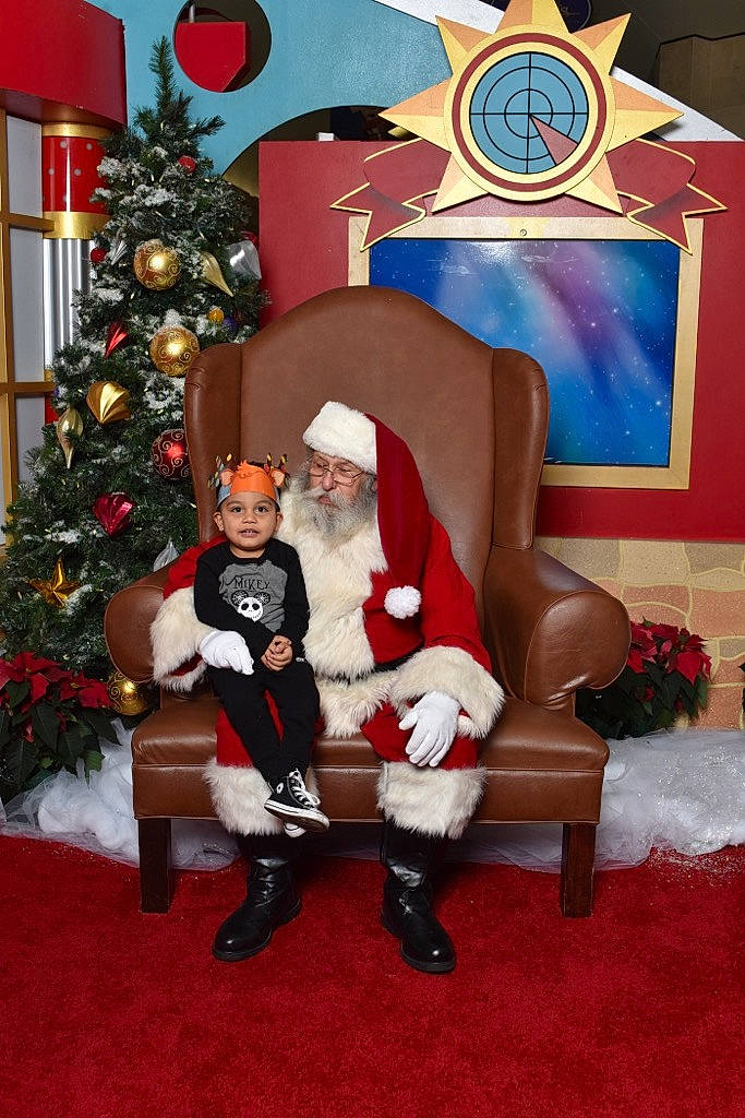 Mikey is registered to the contest to win money with this photo: christmas, christmas_ornament, christmas_tree, event, fictional_character, fun, hat, headwear, holiday, holiday_ornament, human_body, human_leg, knee, lap, leg, ornament, person, plant, santa_claus, smile