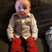 Jaxon is registered to the contest to win money with this photo: baby, infant, child, sofa, couch, vest, button_up_shirt, red_pants, socks, sitting, portrait, wide_eyes, curly_hair, living_room, fabric, cute, expression, hands, legs, seat