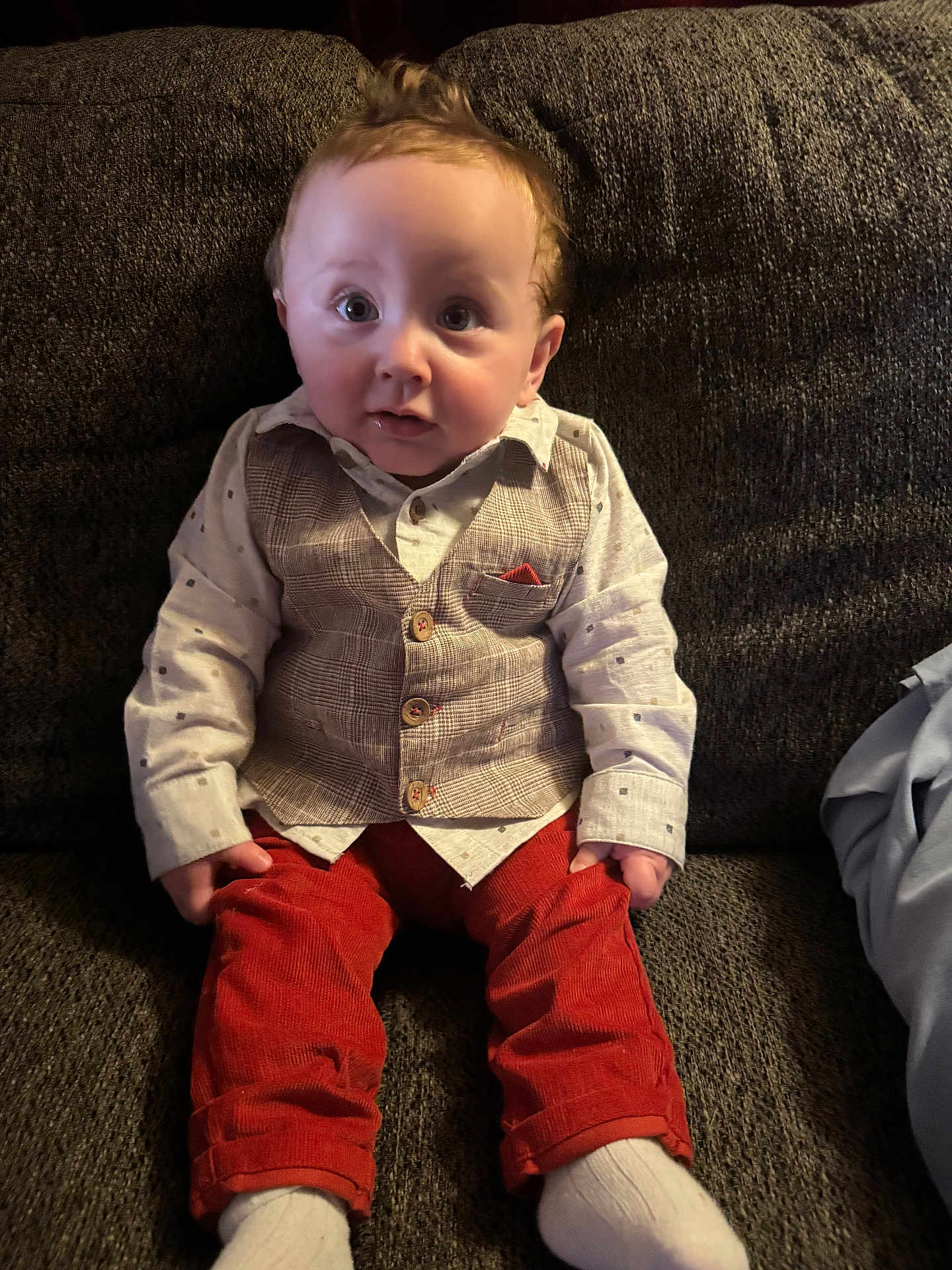 Jaxon is registered to the contest to win money with this photo: baby, infant, child, sofa, couch, vest, button_up_shirt, red_pants, socks, sitting, portrait, wide_eyes, curly_hair, living_room, fabric, cute, expression, hands, legs, seat