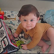 Oliver is registered to the contest to win money with this photo: baby, child, onesie, crawling, playmat, toy, patterned, blanket, indoor, curious, blue, mustard, infant, face, person, young_child, cute, smiling, bright_eyes, colorful