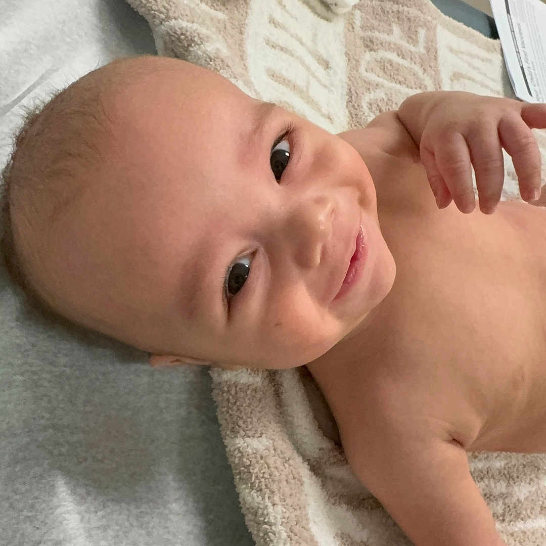 Ziven is registered to the contest to win money with this photo: baby, blanket, cheerful, child, cute, expression, face, furniture, hand, happy, head, indoor, infant, lying_down, person, room, skin, smiling, towel, young