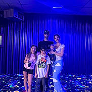 Ziven is registered to the contest to win money with this photo: baby, blacklight, blue_light, carpet, casual_clothing, child, family, floor, fun, group, happy, indoor, man, pattern, people, portrait, smile, space_theme, standing, woman