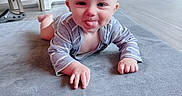 Ethan is registered to the contest to win money with this photo: baby, child, tongue_out, carpet, indoor, floor, blue_wall, chair, furniture, smiling, crawling, person, cute, playful, infant, clothing, light, head, hands, expression