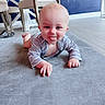 Ethan is registered to the contest to win money with this photo: baby, child, tongue_out, carpet, indoor, floor, blue_wall, chair, furniture, smiling, crawling, person, cute, playful, infant, clothing, light, head, hands, expression