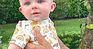 Ethan is registered to the contest to win money with this photo: baby, child, blue_eyes, onesie, hand, watch, outdoor, greenery, garden, person, infant, cute, smiling, skin, portrait, nature, holding, short_sleeves, daylight, human