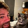 Duchess is registered to the contest to win money with this photo: man, beard, smile, cat, gray_cat, indoor, bed, blanket, furniture, dresser, television, curtains, relaxed, portrait, face, pet, animal, human, cozy, room