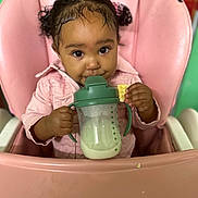 Alejandra joined the competition — help win amazing prizes! toddler, child, baby, high_chair, pink, sippy_cup, milk, cracker, curly_hair, pigtails, cute, indoors, feeding, small_hand, face, portrait, clothing, jacket, seat, table