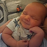 Bentley is registered to the contest to win money with this photo: newborn, baby, infant, sleeping, smiling, face, portrait, close_up, onesie, stars, arms, hands, blanket, pillow, couch, indoor, home, cozy, cuddled, photography