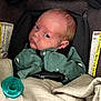 baby, blanket, car_seat, child, closeup, clothing, comfort, cute, expression, face, green_pajamas, head, indoors, infant, newborn, pacifier, person, safety, sitting, warning_label