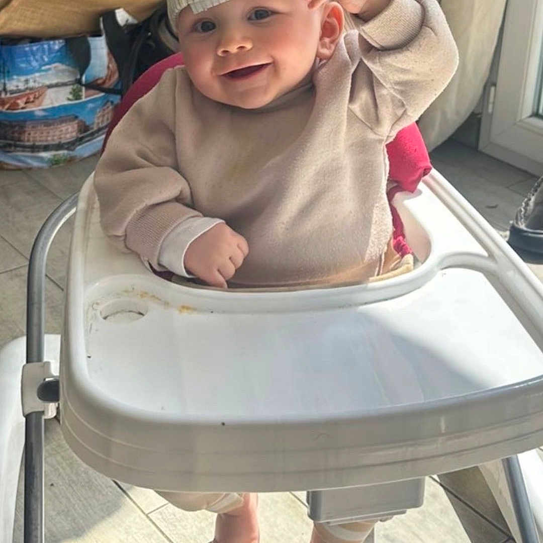 Ezekyel participe au concours pour gagner de l'argent avec cette photo : baby, high_chair, cap, smile, indoor, sunlight, sweater, footwear_free, floor_tiles, curtains, bag, child, person, happy, cute, headwear, shadow, window, home, casual