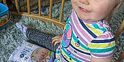 Grace is registered to the contest to win money with this photo: toddler, child, baby, smiling, headband, striped_clothing, blue_eyes, sitting, rug, baby_wipes, doll, wooden_baby_gate, indoor, play_area, cute, happy, colorful, soft_texture, person, young_child