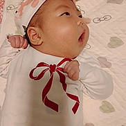 Aisha joined the competition — help win amazing prizes! baby, infant, headband, white_clothing, red_bow, fist, lying_down, quilt, patterned_background, cute, child, newborn, soft_lighting, indoors, portrait, face, cheeks, expression, small_hands, sleepwear