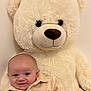 baby, teddy_bear, smile, plush_toy, soft, cozy, child, cute, indoor, light_background, portrait, happy, infant, clothing, warm_colors, furniture, toy, head, face, cuddle